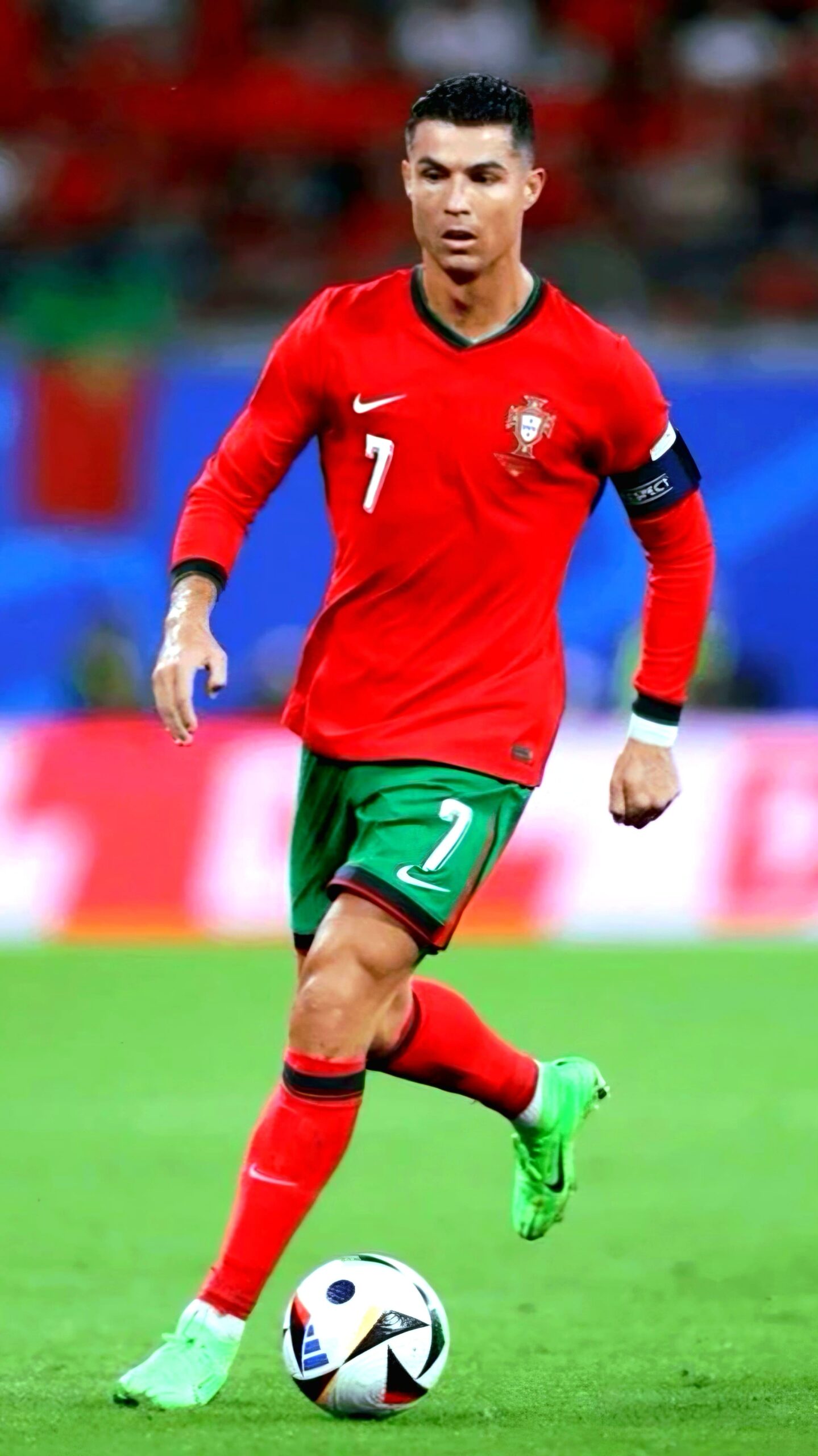 A soccer player in a red jersey with the number 7, green shorts, and green shoes runs on the field, mid-game, with a ball at his feet. He wears a black captain's armband. For fans wanting to catch every moment live from home, don’t miss out—purchase IPTV and stay connected to all the action.