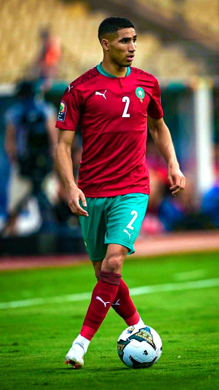 A soccer player in a red and green uniform with number 2 dribbles a ball on a field during a match, an exciting moment you can watch live when you purchase IPTV.